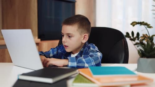 Süßes männliches Kind, das in einem gemütlichen Zuhause sitzt und sich ein Bildungsvideo auf dem Laptop ansieht