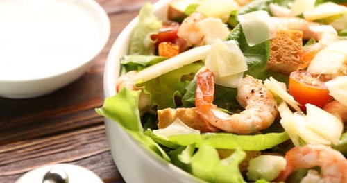 Délicieuse salade César aux crevettes dans un bol sur une table en bois, gros plan. La caméra se déplace vers la droite