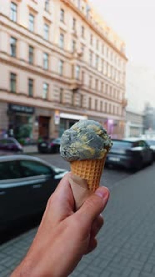 Una mano sostiene un delicioso cono de helado de chocolate y vainilla mientras pasea por una ajetreada ciudad