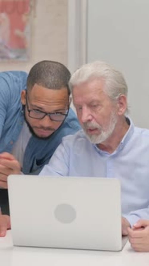 Senior Man Using Laptop with Younger Man Assisting