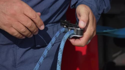 Gros plan sur les mains d'un homme manipulant une corde dans la poulie du harnais de sécurité
