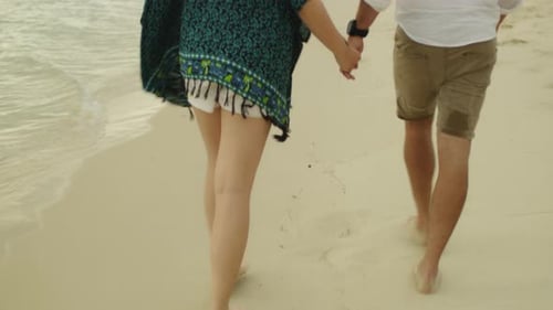 Young Couple Holding Hands and Walking Along the Beach Near the Water