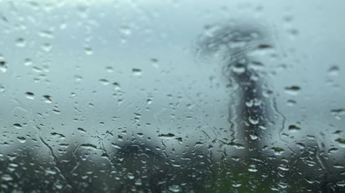 Raindrops trickling down on wet clear car window glass during heavy rain against beach view , people