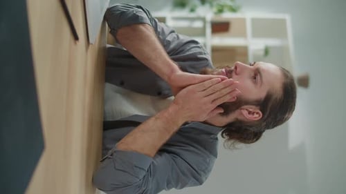 Bearded Man Resting Face in Hands at Desk