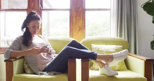Woman Relaxes in Armchair Using Smartphone