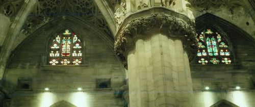 Powerful columns with stucco and sculptures, tall arched stained glass windows in cathedral church.