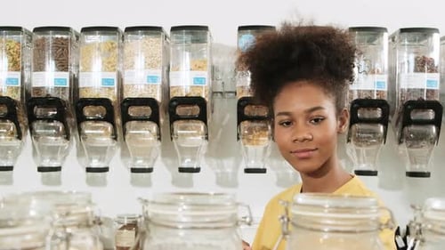 A young woman is shopping in refill store with reusable bag, zero-waste grocery.