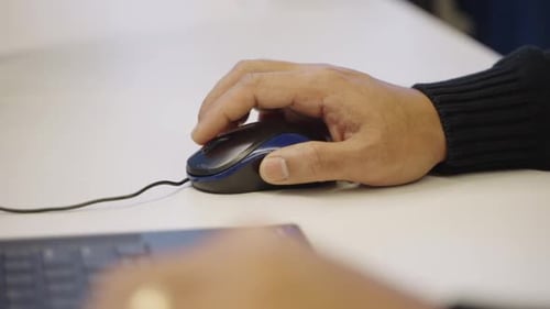 Close up of anonymous man's hands scrolling mouse wheel next to laptop in an office