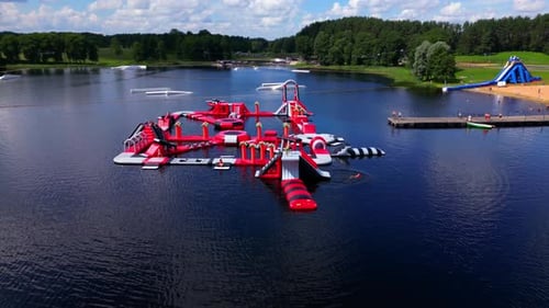 Zarasai Water Park Close-Up with red inflatables on lake, with swimmers, pier, and forest backdrop
