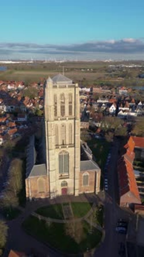 Aerial view of a historic town with a tall Gothic church in the center. Red-roofed houses