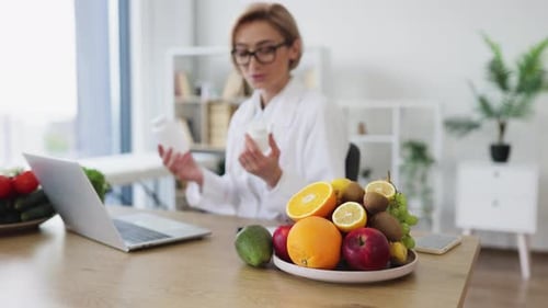 Woman in Lab Coat Talking About Pills and Fruit