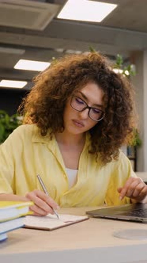 Focused University Student Studying and Taking Notes Using Laptop