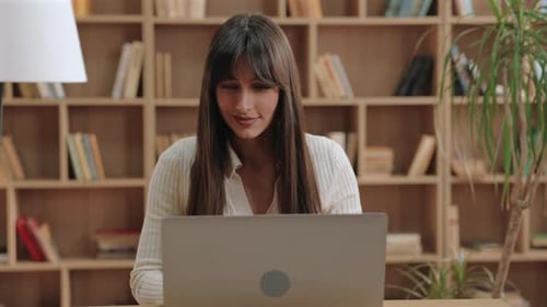 Woman Working on Laptop in Room with Bookshelves