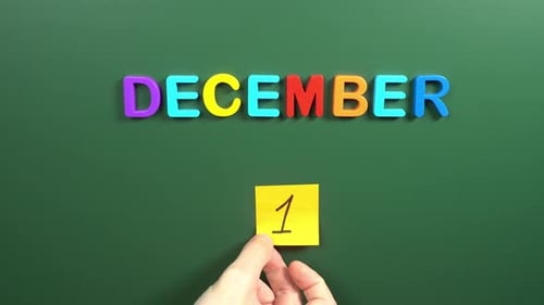 Hand sticking a sticker 1 December calendar day on school board. 1 date of December. First day