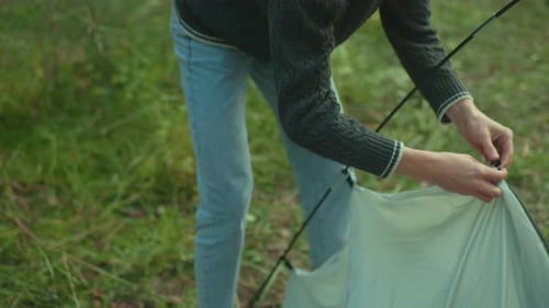 Tourist Standing While Securing Tent Fabric Under Sunlight in Forest