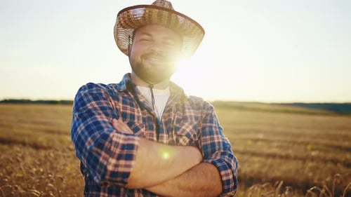 Happy Bearded Farmer in Cap Looking at Camera Standing on Agricultural Wheat Field with Combine