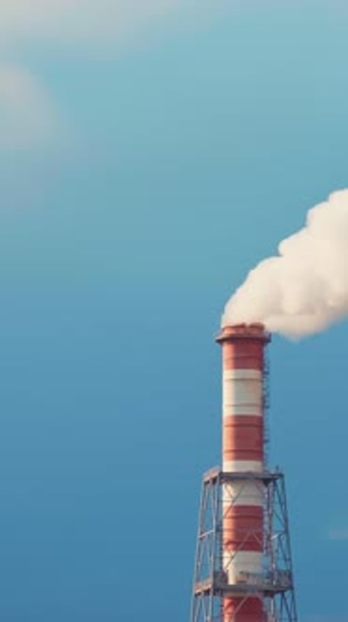 Una chimenea de una central térmica y eléctrica emite humo blanco en el cielo azul, calentando energía de producción de energía