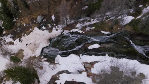 Waterfalls Flowing On The Rocky Cliff To The Stream With Ice And Snow In Winter. - aerial shot