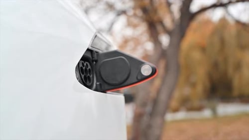 Slow motion close view of a man plugging charger into an electric car charging port