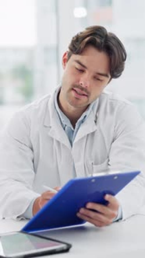Young Adult Doctor Writing on Clipboard in Office
