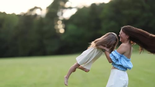 Mother Lifting Her Daughter While Spinning Together in a Sunny Green Park