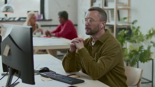 Businessman in Earbuds Video Calling on Computer in Modern Office