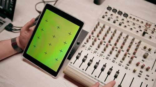 professional recording studio sound engineer holding tablet with green screen near equalizer mixer