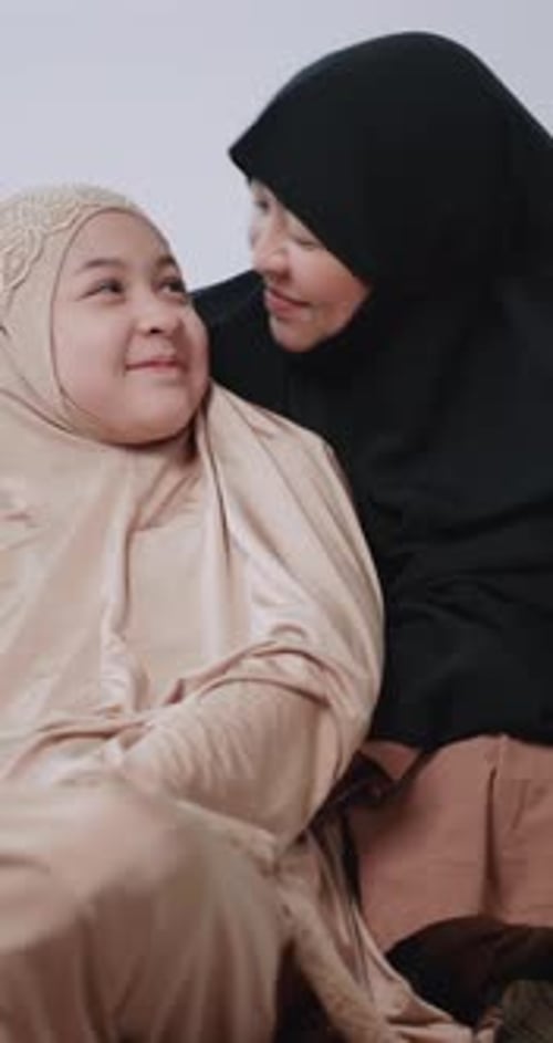 Muslimische Mutter und Tochter im Hijab-Kleid haben Spaß daran, sich zu Hause zu umarmen und zu küssen.