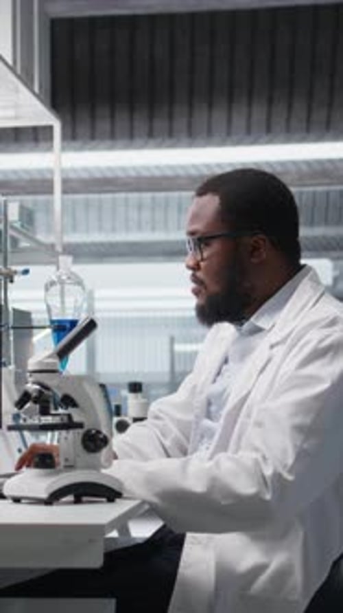 Scientist uses microscope in laboratory with colleague