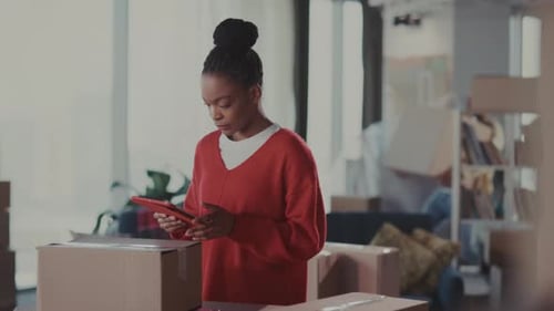 Woman Using Tablet Near Moving Boxes in Apartment