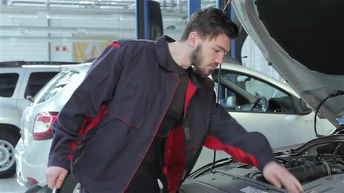 Focused Mechanic Inspects Car Engine at Service Station