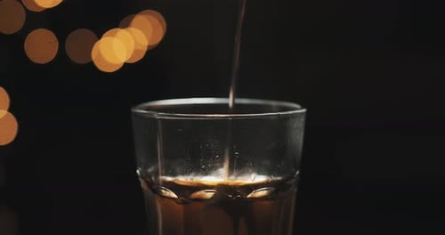 Pouring tea into the cup with teapot. Hot tea. Close up. Bubbles. Glass cup with blur lights on the
