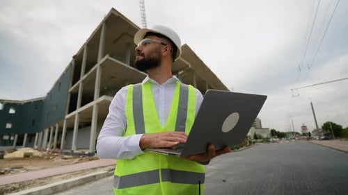Construction Manager Engineer Inspecting Building Site with Laptop