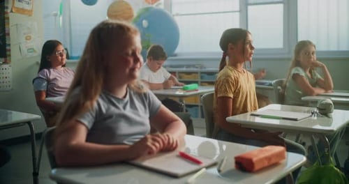Primary School Children Sitting at the Desks Listening to Lecture Raising Hands to Give Correct