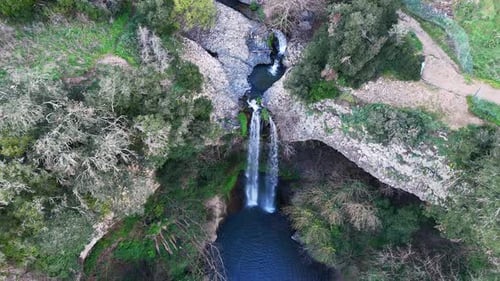 Enchanting Waterfall Cascading Down Rocky Cliffs Surrounded by Lush Greenery at Dusk.