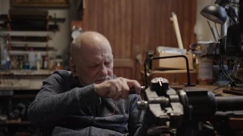 Mestre joalheiro idoso sênior em cadeira de rodas trabalha em uma oficina