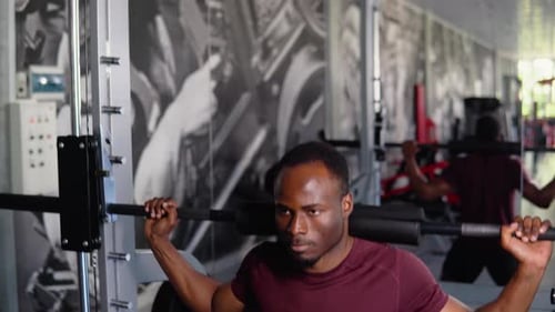 African American Bodybuilder Doing Squats Using a Barbell in a Gym to Train His Legs and Back