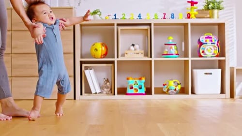 Mom helping and support baby learn to walk with love indoors at home. First steps of baby learning w