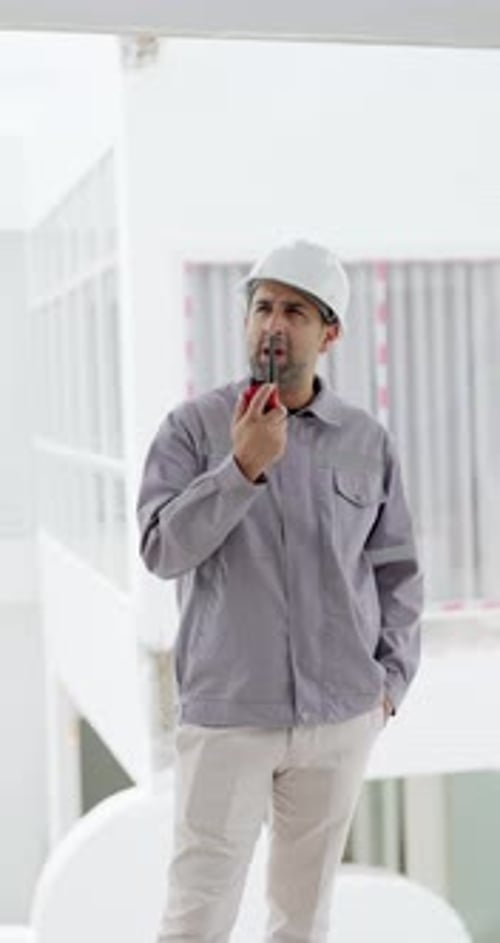 Asian male manager uses radio while standing inside unfinished building, coordinating construction