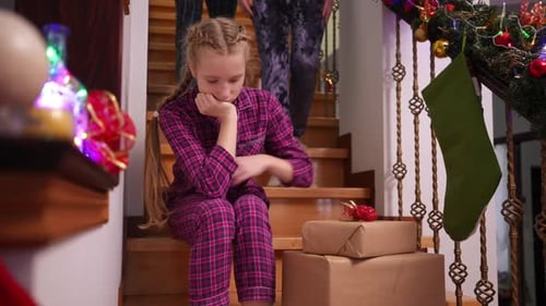Sad Teen Girl Sitting on Stairs with New Year Gifts As Man and Woman Walking Downstairs Calming Down