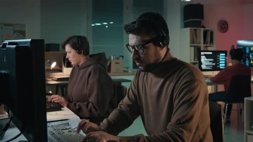 Estafador masculino escribiendo en la computadora mientras habla con la víctima en un centro de llamadas fraudulentas