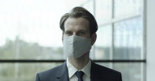 Man in Suit Wearing Mask Standing by Window