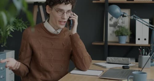 Portrait of Cheerful Worker Speaking on Mobile Phone and Working with Laptop in Modern Office
