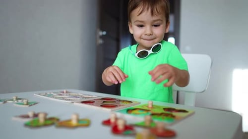 Lovely boy in green t-shirt sitting at the desk at home playing with toys.