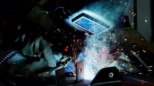 Professioneller Schweißer, der in der Fabrikwerkstatt der Fabrik arbeitet, mit einem männlichen Techniker beim Schweißen