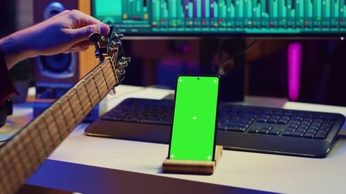 Man Tunes Guitar Near Phone With Green Screen