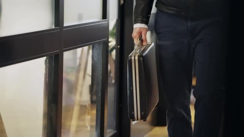 Man walking with a black briefcase in hand, wearing a leather jacket and jeans. Business, travel.
