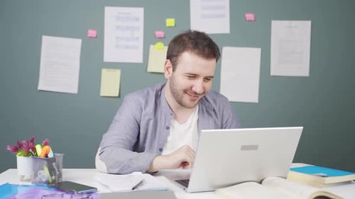 Young Adult Male Works on Laptop at Desk