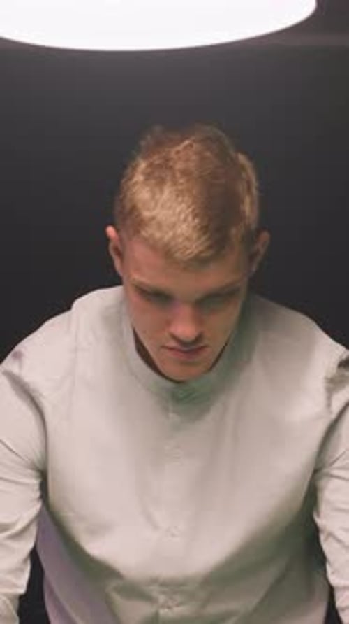 Gros plan d'un jeune homme en chemise blanc cassé avec une concentration calme sur fond sombre