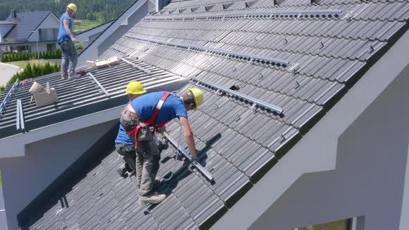 Static side view showing workers on the slope of the roof, drilling the ...
